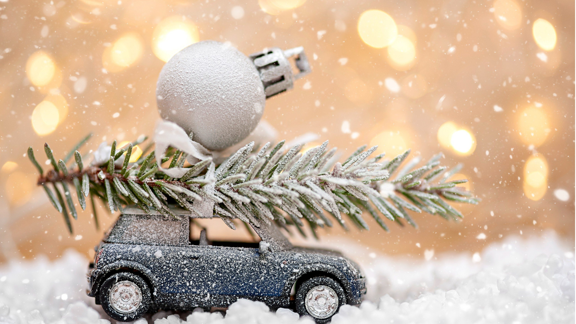 dunkles spielzeugauto mit christbaum und christbaumkugel am dach steht auf kunstschnee